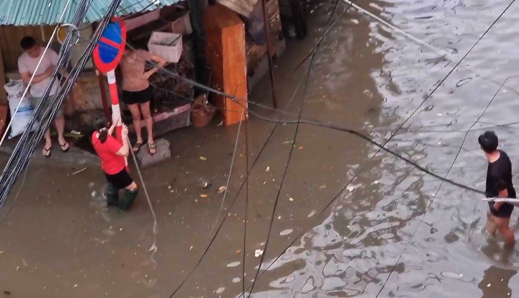 Nước ngập ngang bắp chân ở ngõ nhà chị Thanh sau trận mưa chiều 29/5, một người mang đồ đạc ra chặn không cho ôtô đi vào ngõ, tránh tạo sóng nước. Ảnh: H.T.